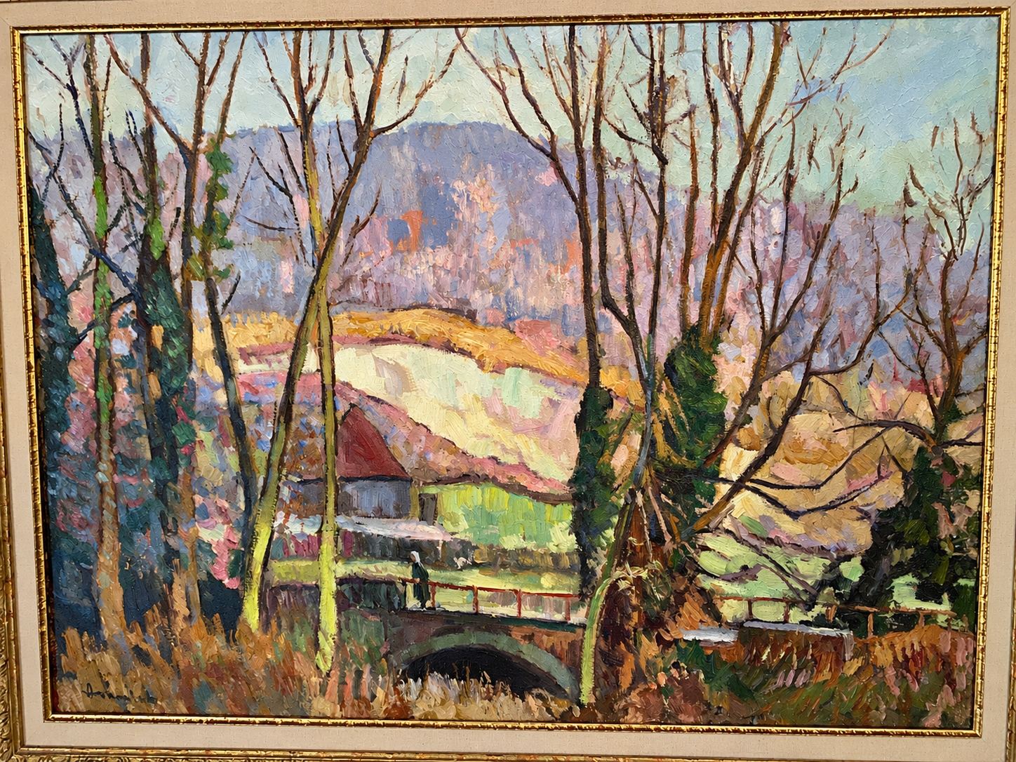 Tableau encadré à l'huile représentant un paysage d'hiver avec des arbres sans feuilles, un petit pont de pierre, une maison au toit rouge et des collines en arrière-plan.
